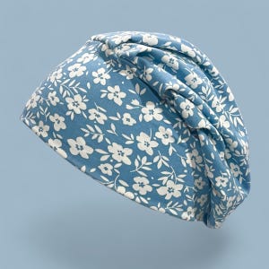Puede incluir: Un gorro azul con estampado floral blanco. El gorro presenta un diseño de flores y hojas blancas. La tela es suave y el gorro tiene un diseño fruncido. Un accesorio de moda.
