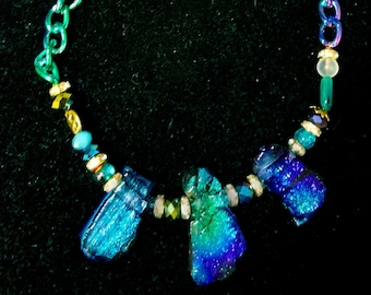 May include: A necklace with a gold chain and blue and green glass beads. The necklace has a pendant with three large, iridescent blue and green glass pieces.