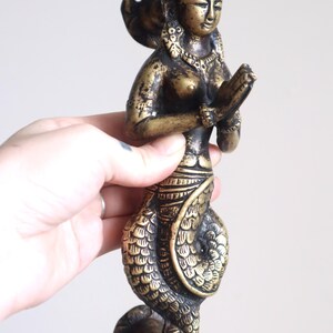 May include: A bronze-colored mermaid door handle. The sculpture features a woman with clasped hands, a detailed headdress, and a scaled tail. The handle is approximately 8 inches in height.