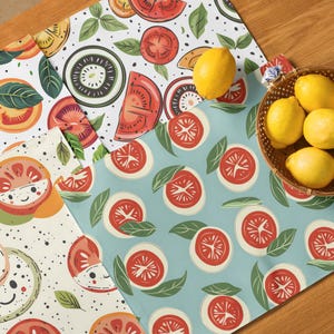 May include: A collection of colorful kitchen textiles featuring fruit and vegetable designs. The textiles include patterns of tomatoes, kiwi, and lemons. A woven basket holds several fresh lemons. The textiles are on a wooden surface.