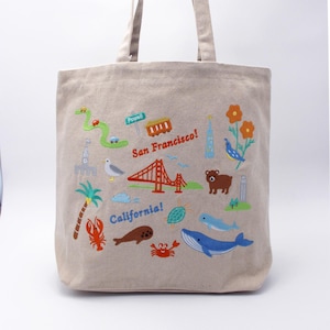 May include: Beige tote bag with colorful embroidered illustrations of San Francisco landmarks and California imagery. Features the Golden Gate Bridge, a cable car, a bear, a whale, and the text "San Francisco!" and "California!"