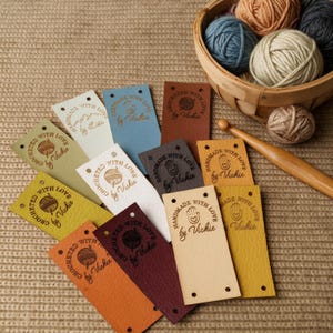 Peut inclure: Une collection d'étiquettes rectangulaires en similicuir de différentes couleurs, notamment crème, bleu, marron, jaune et orange. Chaque étiquette présente un logo circulaire en creux avec le texte "Handmade with Vickie" ou "Crocheted with Vickie".