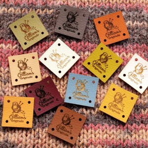 Peut inclure: Assortiment de 12 étiquettes en cuir avec une petite illustration d'une pelote de laine et d'aiguilles à tricoter. Chaque étiquette porte l'inscription "Gillian's Originals" en lettres dorées.