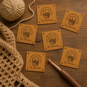 Può includere: Cinque etichette quadrate color cuoio con quattro fori agli angoli, ciascuna con una grafica nera di un cestino di lana e il testo "CROCHET WITH LOVE by Sammy". Un gomitolo di lana e un uncinetto marrone sono accanto alle etichette.