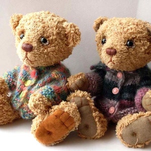 May include: Two brown teddy bears wearing knitted sweaters. The bear on the left is wearing a multi-colored sweater with a yellow button. The bear on the right is wearing a purple and black striped sweater with pink buttons.