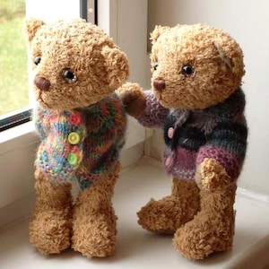 May include: Two brown teddy bears wearing knitted sweaters. The bear on the left is wearing a multi-colored sweater with buttons. The bear on the right is wearing a purple and blue sweater.