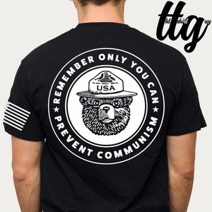 May include: Black t-shirt with a white circle graphic on the back. The graphic features a bear wearing a ranger hat with "USA" on it. The text around the bear reads "Remember Only You Can Prevent Communism".