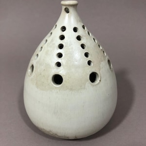 Könnte beinhalten: Eine weiße Keramikvase mit birnenförmigem Körper und einer runden Öffnung oben. Die Vase hat eine Reihe kleiner Löcher um den Körper herum.