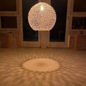 May include: A round, woven, light fixture hangs from the ceiling, casting a circular pattern of light on the carpet below.