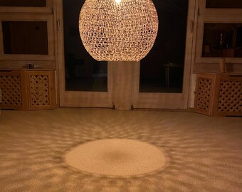 May include: A round, woven, light fixture hangs from the ceiling, casting a circular pattern of light on the carpet below.