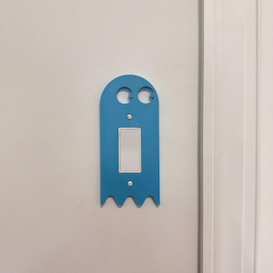 May include: A light blue ghost-shaped light switch cover with two round cutouts for eyes and a white light switch plate.