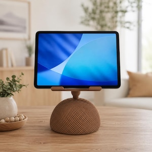 May include: A tablet computer mounted on a brown, dome-shaped stand with a textured, cross-hatched grid pattern. The tablet screen displays a vibrant blue abstract background with light blue and dark blue curved shapes.