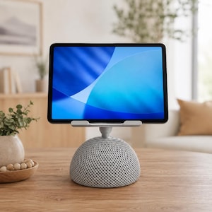 May include: A tablet computer mounted on a light gray, dome-shaped stand with a textured, lattice-like pattern. The tablet screen displays a vibrant blue abstract graphic with curved lines. The stand features a central swivel joint.
