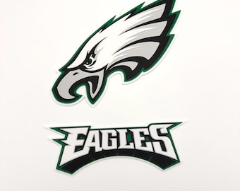 May include: Two-piece set featuring the Philadelphia Eagles logo. The top piece is a stylized eagle head in white, gray, and black with green trim. The bottom piece reads "EAGLES" in white letters with a black and green border.