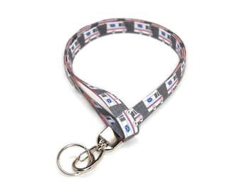 May include: A gray lanyard with a repeating pattern of white mail trucks. The lanyard has a silver key ring attached.