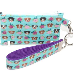 May include: A turquoise zippered pouch with a floral pattern featuring a dog's face. The pouch has a purple strap with a silver key ring.