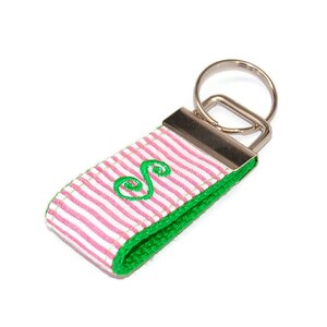 May include: A pink and white striped key chain with a green embroidered letter "S" and a silver key ring.