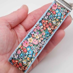 May include: A light blue key chain with a floral pattern. The fabric is black with a variety of colorful flowers.