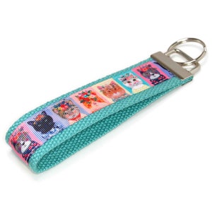 May include: Teal blue key chain with a colorful ribbon featuring a pattern of cats with flowers. The ribbon is attached to a silver key ring.