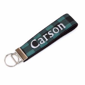 May include: A black and green plaid keychain with the name "Carson" embroidered in white. The keychain has a silver metal ring.