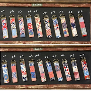 May include: Ten rectangular fabric key fobs with bronze-toned metal hardware and split rings, arranged in two rows labeled front and back. Each fob features a unique patchwork of colorful floral, geometric, and polka dot patterns in various colors.