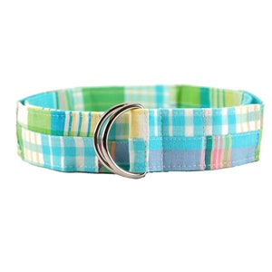 May include: A colorful plaid belt with a silver double-ring buckle. The belt features a patchwork design with shades of blue, green, yellow, and pink. The belt is made of fabric and is designed to be worn around the waist.