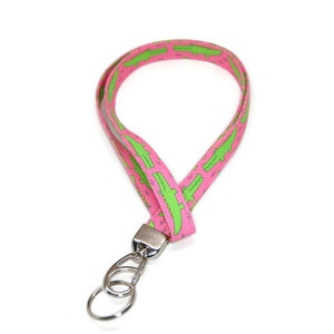 May include: Pink lanyard with a green alligator print and a silver swivel clip and key ring.