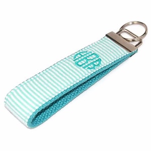 May include: A turquoise and white striped key chain with a silver key ring. The key chain has a turquoise monogram in the center.