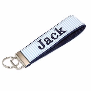 May include: A blue and white striped key chain with a silver key ring. The keychain has the name "Jack" embroidered in navy blue.