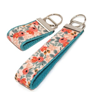 May include: Two teal and pink floral patterned keychains with silver key rings.