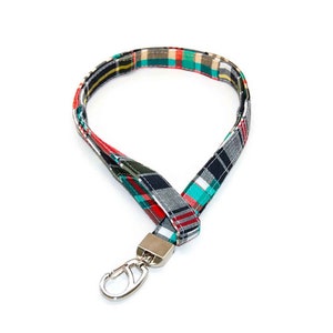 May include: A colorful plaid lanyard with a silver swivel clip. The lanyard is made of fabric and has a red, green, black, and white plaid pattern.