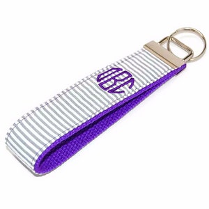 May include: A white and gray striped key chain with a purple monogram "ABC" and a silver key ring.