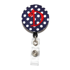 May include: A navy blue and white polka dot button with a red embroidered letter "D" attached to a retractable badge holder.