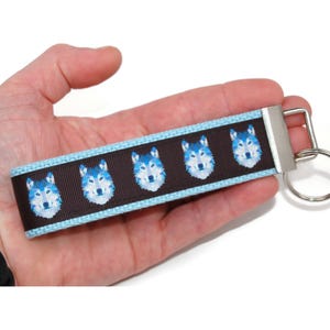 May include: A brown and blue key chain with a repeating pattern of wolf faces. The key chain has a silver metal key ring.