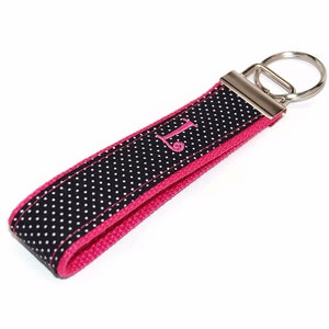 May include: Black and white polka dot key chain with a pink border and a silver key ring. The keychain is personalized with the letter "L" in pink.