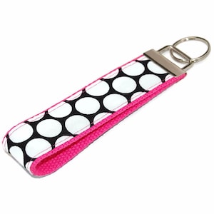 May include: A black and white polka dot key chain with a pink trim and a silver key ring.
