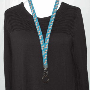 May include: A teal blue lanyard with a pattern of small brown dogs. The lanyard has a silver swivel clip and a silver ring.