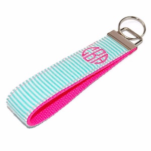 May include: A turquoise and white striped key chain with a pink backing. The keychain has a silver key ring and a pink monogram.