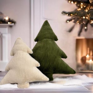May include: Two plush Christmas tree pillows, one in a cream color and one in a dark green color. The pillows are made of a soft, textured fabric and are perfect for adding a festive touch to your home decor.
