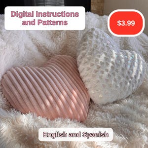 Könnte beinhalten: Zwei herzförmige Kissen, eines rosa mit vertikalen Streifen und eines weiß mit einer strukturierten Oberfläche. Die Kissen liegen auf einer flauschigen weißen Oberfläche. Der Text "Digital Instructions and Patterns" befindet sich oben im Bild, und der Text "English and Spanish" unten. Der Preis 3,99 € ist in einem roten Kreis oben rechts.