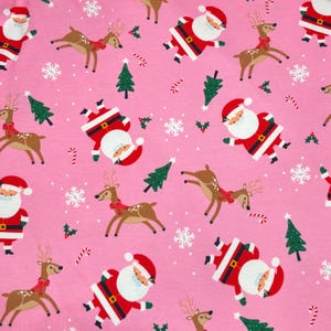 Op de afbeelding: Roze stof met een herhaald patroon van kerstmannen, rendieren, sneeuwvlokken, kerstbomen, zuurstokken en hulst. De kerstman draagt een rood pak en hoed met een witte baard. De rendieren hebben rode sjaals.