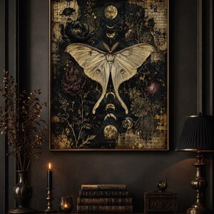 Puede incluir: Una impresi&oacute;n de arte mural rectangular que presenta una gran polilla p&aacute;lida centrada sobre un fondo oscuro y texturizado. La composici&oacute;n incluye fases lunares doradas, elementos florales dispersos y texto tenue, todo en un marco fino.