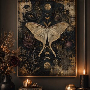 Puede incluir: Un cuadro rectangular que presenta una gran polilla luna p&aacute;lida centrada sobre un fondo oscuro y texturizado. La obra incluye fases lunares en tonos dorados, elementos florales en morado oscuro y negro, y un texto sutil.