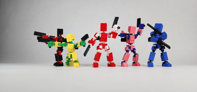 Puede incluir: Cinco figuras de acci&oacute;n articuladas y coloridas posan con armas. Las figuras son rojas, negras, amarillas, rosas y azules. Cada figura tiene una cabeza y un cuerpo en forma de bloque, con articulaciones m&oacute;viles. Est&aacute;n sobre una superficie blanca.