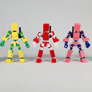 Puede incluir: Se muestran cinco figuras de acci&oacute;n articuladas y coloridas. Cada figura tiene una cabeza y un cuerpo en forma de bloque, con extremidades articuladas. Los colores incluyen rojo, negro, amarillo, verde, rosa y azul. Son juguetes o coleccionables.