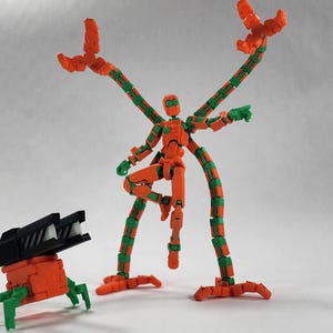 Peut inclure: Figurines articulées orange et vertes. L'une d'elles a plusieurs bras et est en position dynamique. Une figurine plus petite, sur roues, avec un canon noir est également présente. Les figurines sont posées sur un fond uni.