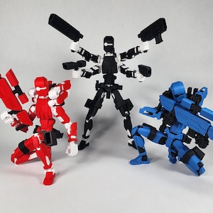 May include: Three articulated action figures, one red, one black, and one blue, each holding a weapon. The red figure is kneeling and holding a large red rifle. The black figure is standing with its arms outstretched, holding two black pistols. The blue figure is kneeling and holding a blue rifle.
