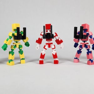 Puede incluir: Cinco figuras de robots articulados y coloridos est&aacute;n en fila. Cada robot es de un color diferente: negro y rojo, amarillo y verde, rojo y blanco, rosa y azul, y azul. Tienen accesorios negros.