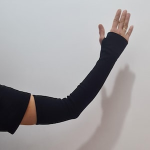 Può includere: Maniche nere con design senza dita. Le maniche si estendono dal polso alla parte superiore del braccio, offrendo copertura. Il tessuto sembra essere un materiale a maglia elasticizzata. Le maniche sono mostrate su uno sfondo bianco.