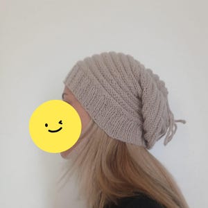 Könnte beinhalten: Beige Strickmütze mit Rippenmuster. Die Mütze ist aus weichem, strukturiertem Garn gefertigt und hat eine leicht lockere Passform. Die Mütze hat eine neutrale Farbe und passt zu verschiedenen Outfits.